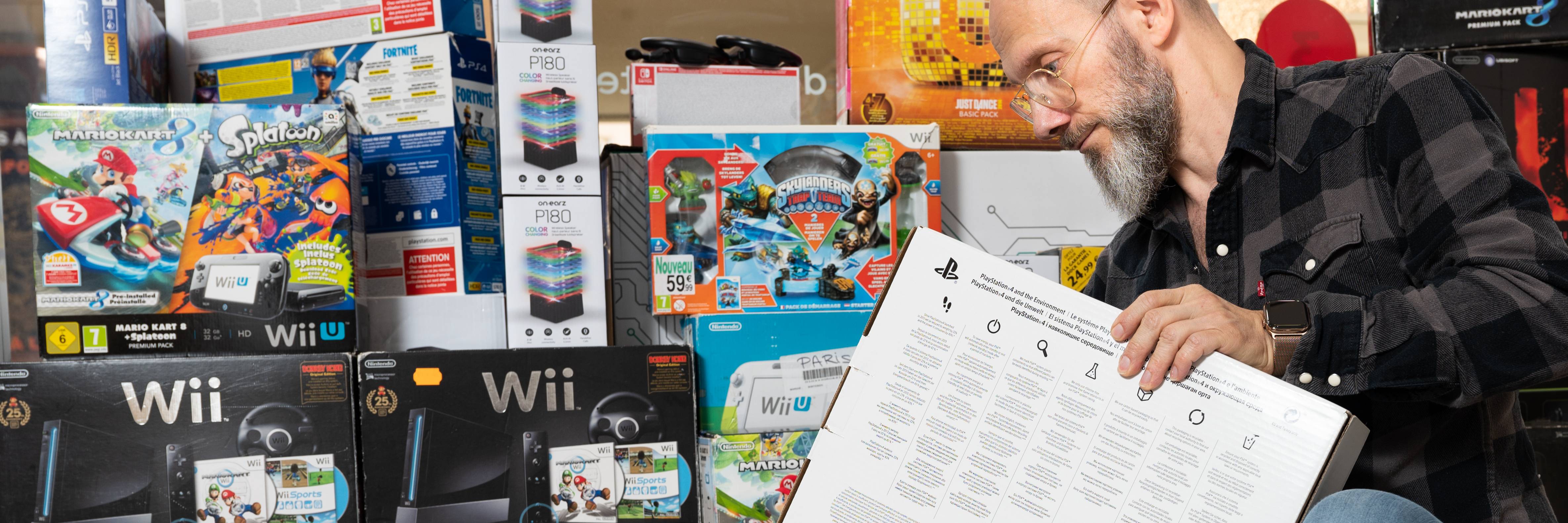 Bannière montrant un des fondateurs d’Olover entouré de nombreuses boîtes de consoles de jeux, illustrant l’engagement dans le gaming responsable et reconditionné